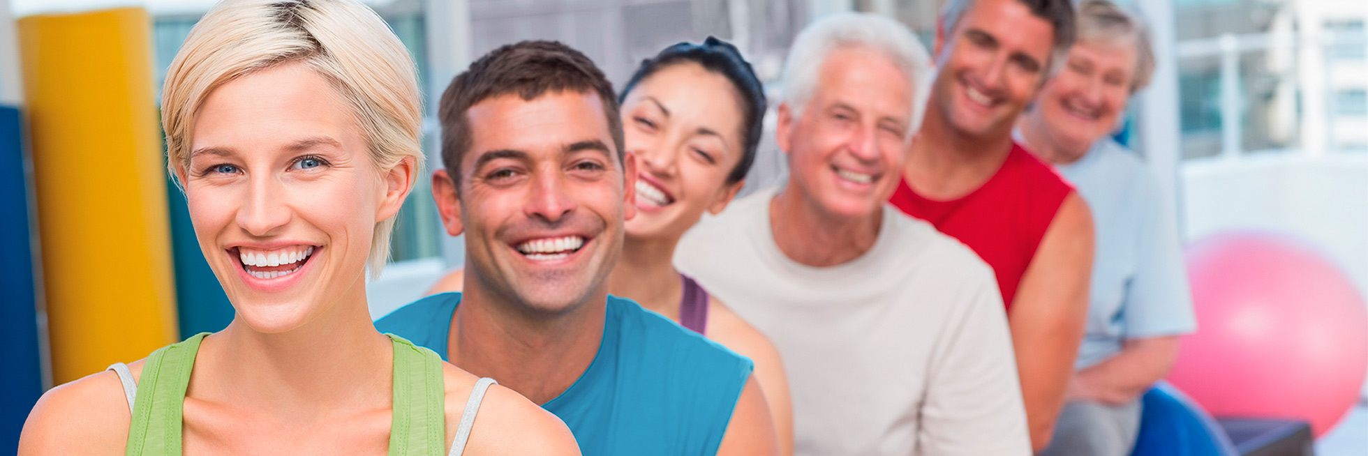 Eine Gruppe strahlender Menschen unterschidlichen Alters und Nationalität im Fitnessraum.